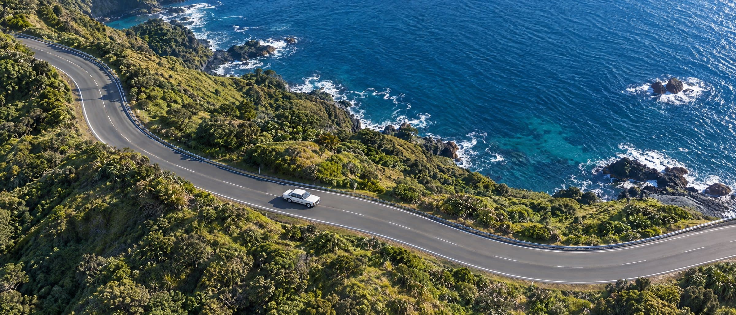 A car on a winding coastal road, seen from above